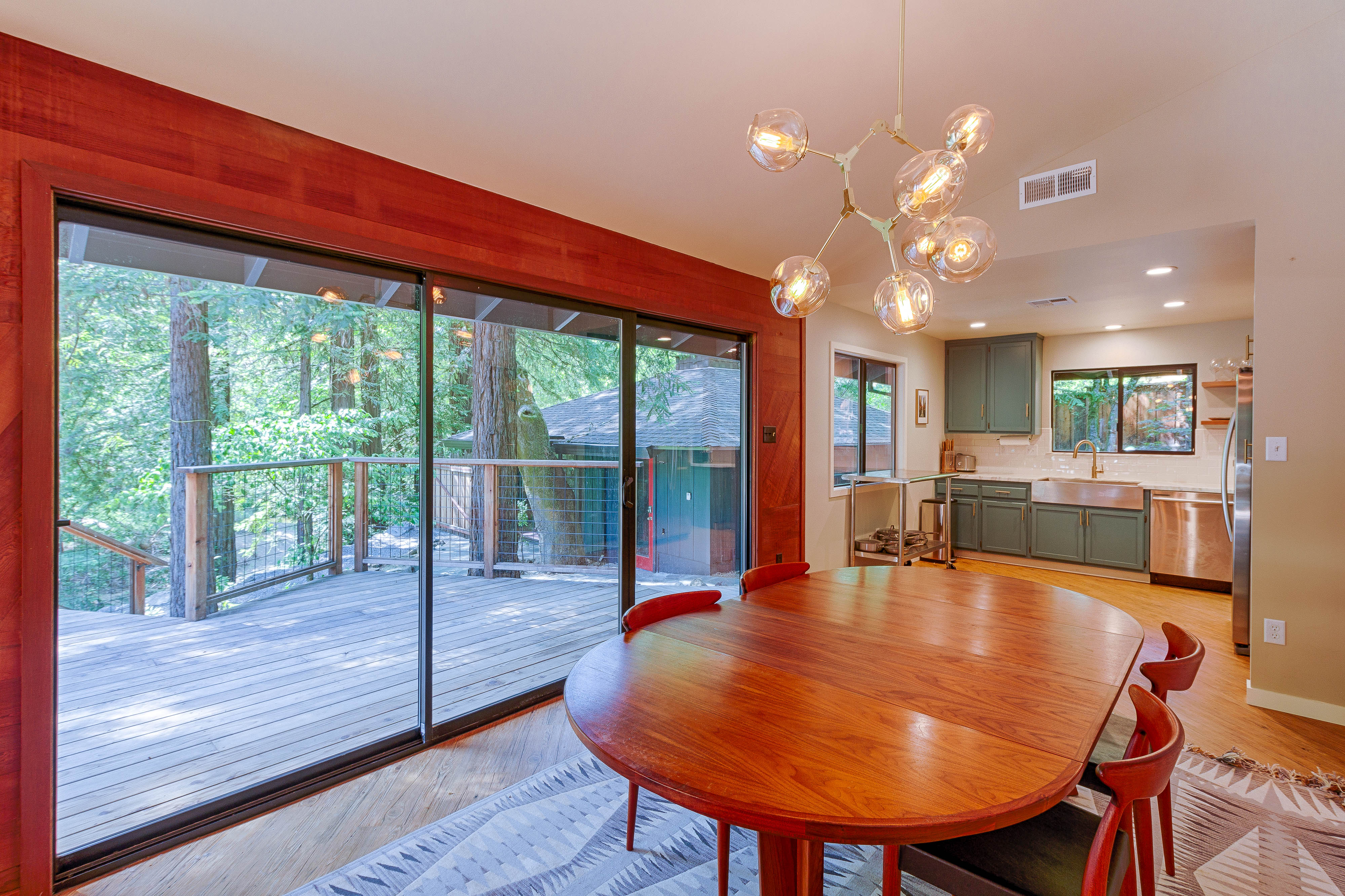 The round redwood dining table beside full-height doors to the trees